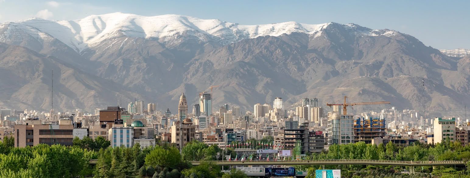 The Tehran skyline of mid-rise towers backed by the snow-capped Alborz mountains, the geographic setting for Iran's sanctioned crypto exchanges and the phishing aimed at their users